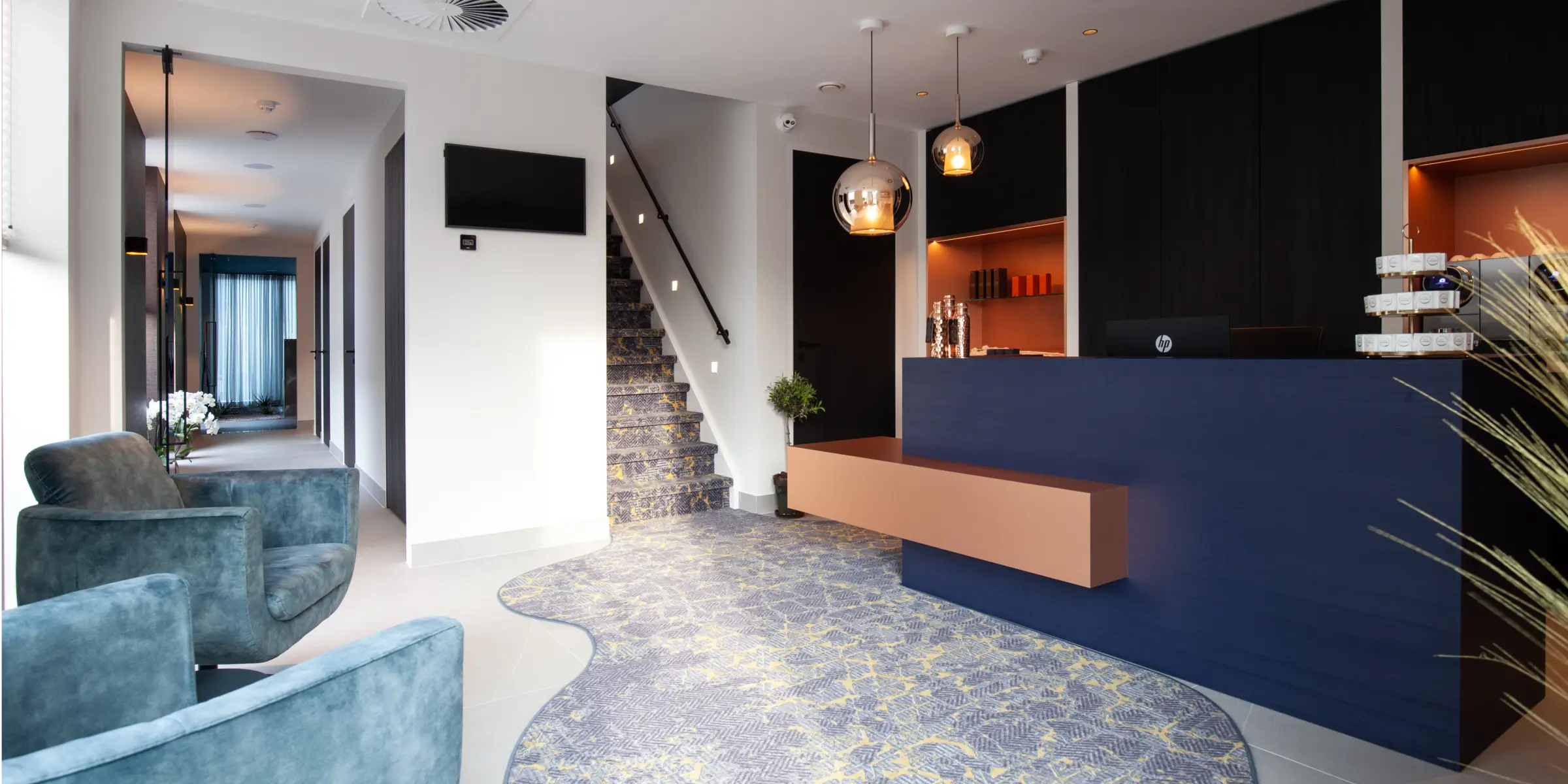 Stilvolle Rezeption und Lounge eines Wellnesszentrums mit modernem Empfang, bequemen Sesseln und Treppe, wo der Duft luxuriöser Aromen Sie beim Betreten sofort begrüßt.